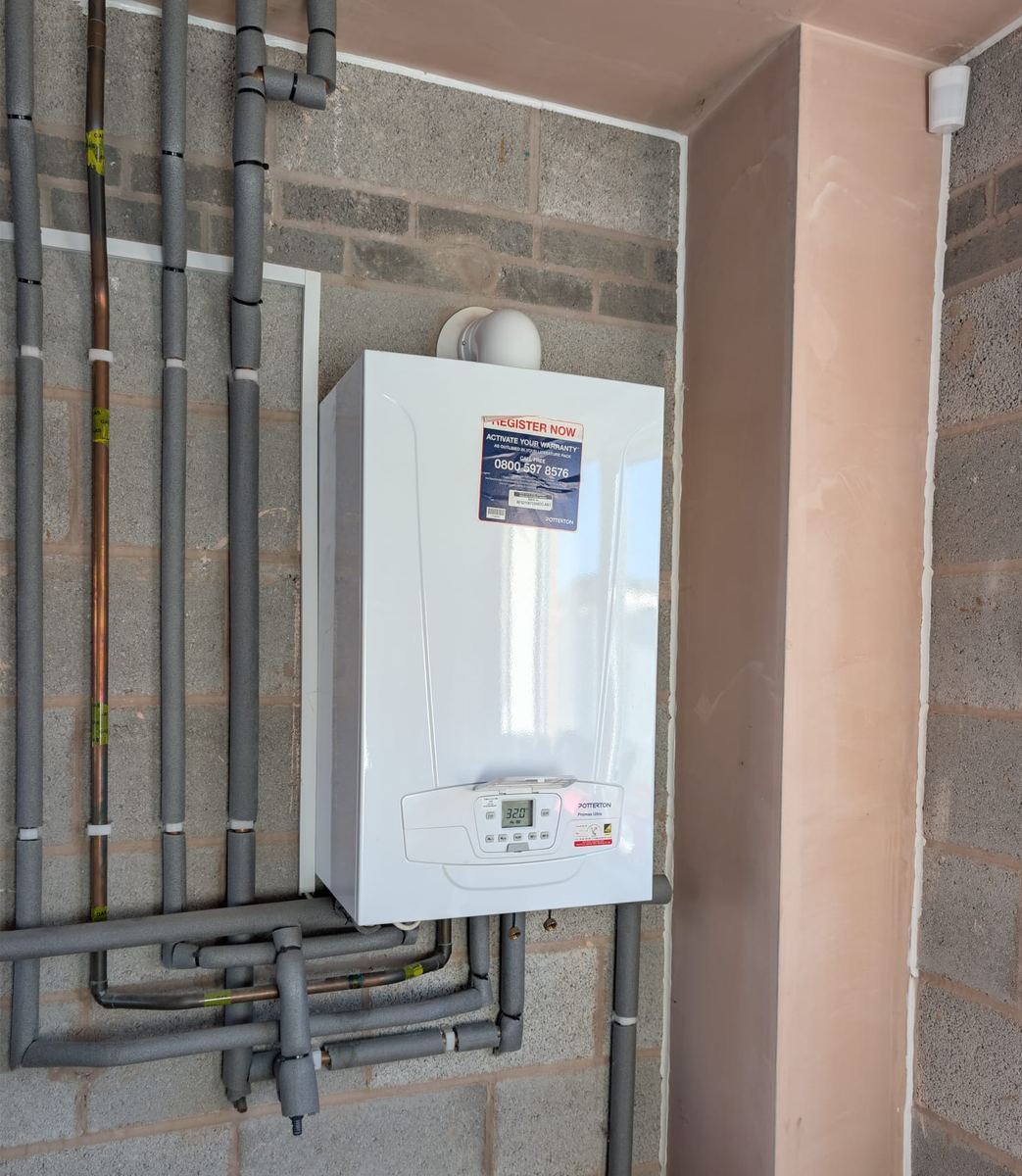 New Potterton Promax Ultra combi boiler fitted on a block wall with insulated pipework run beneath it