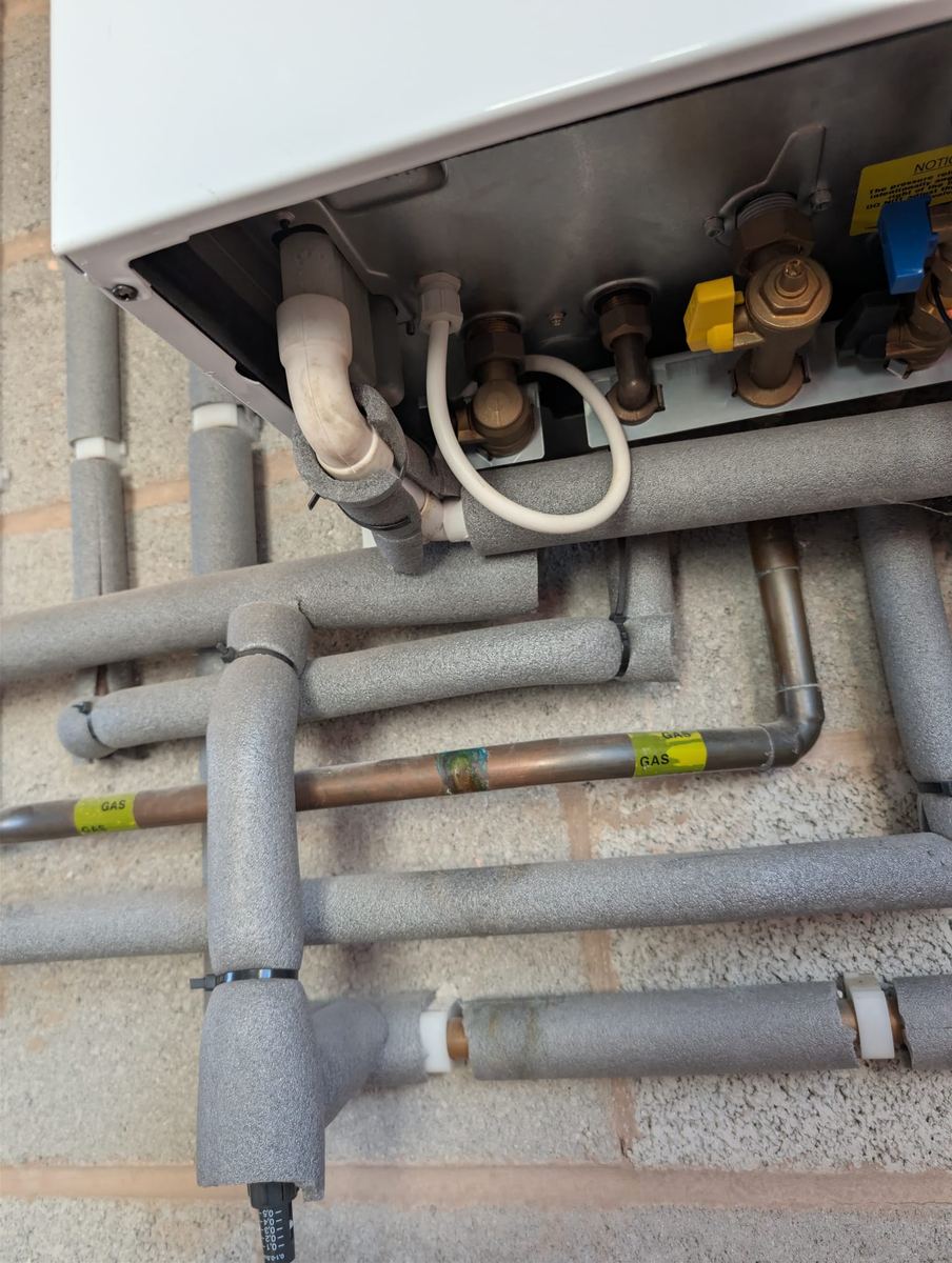 Isolation valves and yellow-labelled gas pipework beneath a newly fitted combi boiler